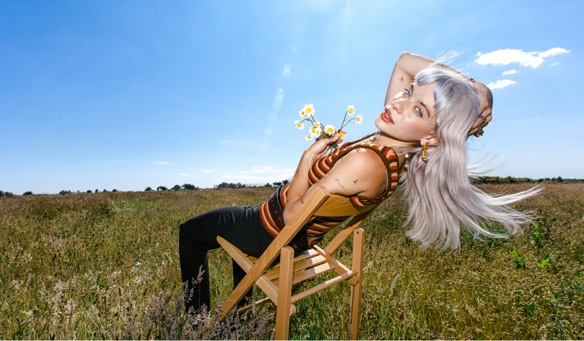 musician Pixie sitting on a chair in a field of grass on a sunny day