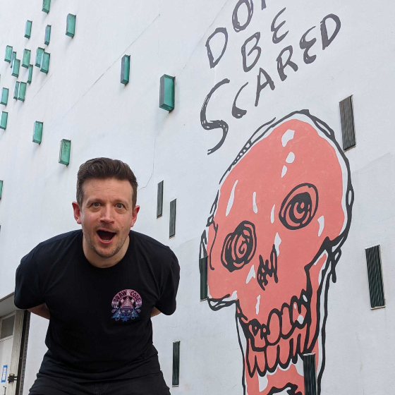 An image of a man next to a wall mural of a red skull.