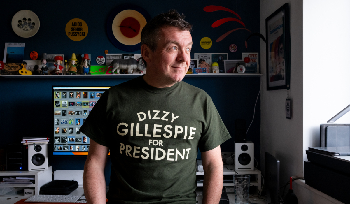 Person wearing a t-shirt that reads "Dizzy Gillespie for President" standing in a room full of collectibles and posters.