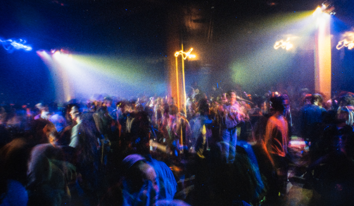 A crowded dance floor with people under colourful lights in a dimly lit club.