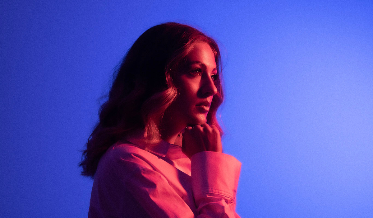 Confident woman stands in front of a mesmerizing blue light, wearing a white shirt.