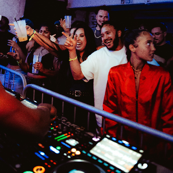 People dancing in a crowd at the barrier od the stage where a DJ is performing.