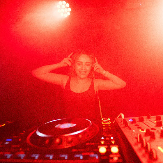 An image of a DJ behing the decks with a red haze over the image..