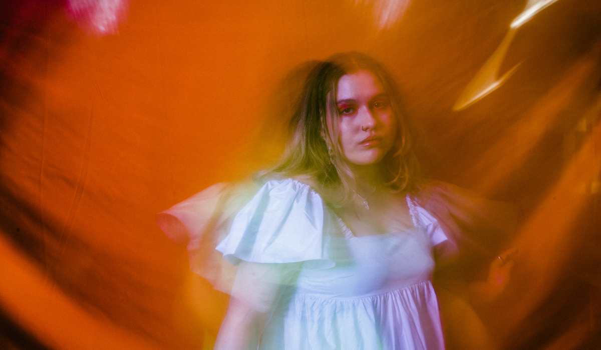 A woman in a white dress poses in front of a bright, multicoloured background.