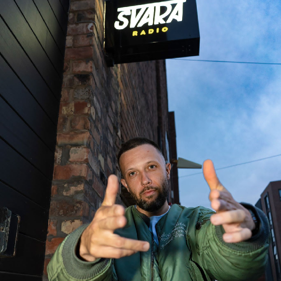 A man gesturing towards a camera outside a music studio.