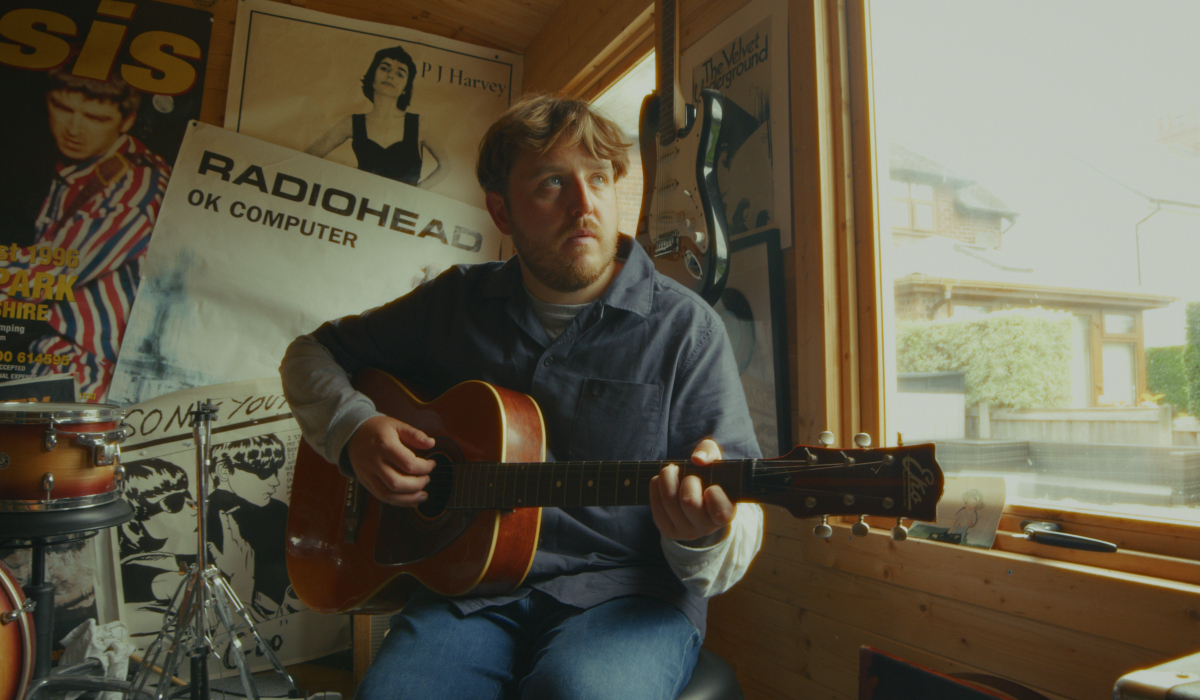 A person playing a guitar in a room where posters for musical bands can be seen on the wall behind them