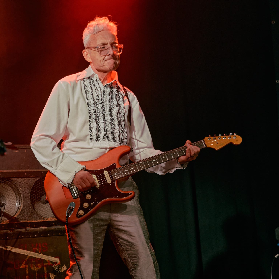 A man playing guitar on stage under a red light