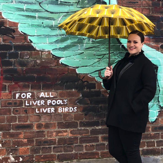 A woman smiling holding a yellow umbrella infront of street art