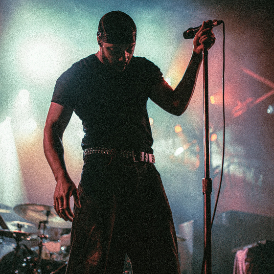 A person perfomring on stage, holding onto the mic with pnk and blue lights behind them