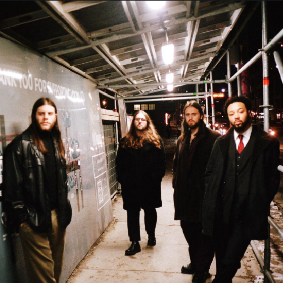 Fout individuals standing under scaffolding outside at night