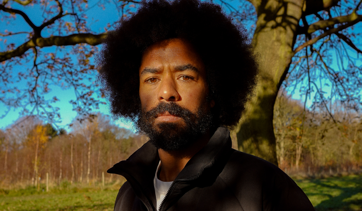 A portrait of a man looking at the camera with trees behind him on a sunny day