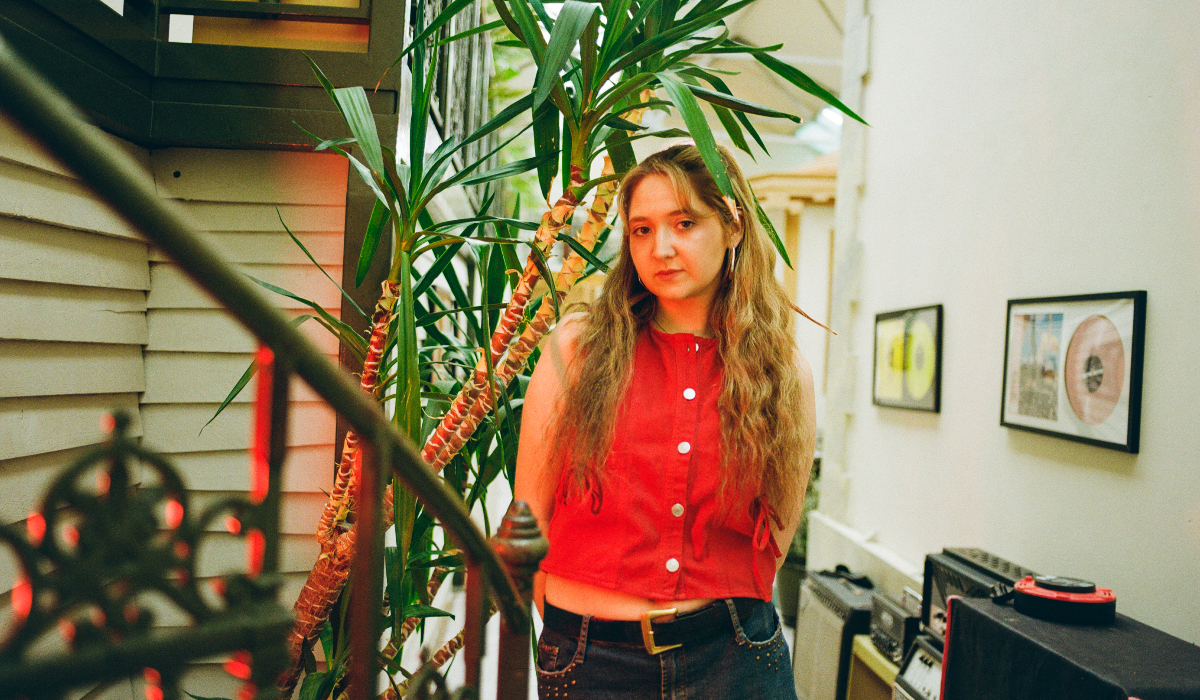 A girl standing in a well-lit room with tall indoor plants behind her.