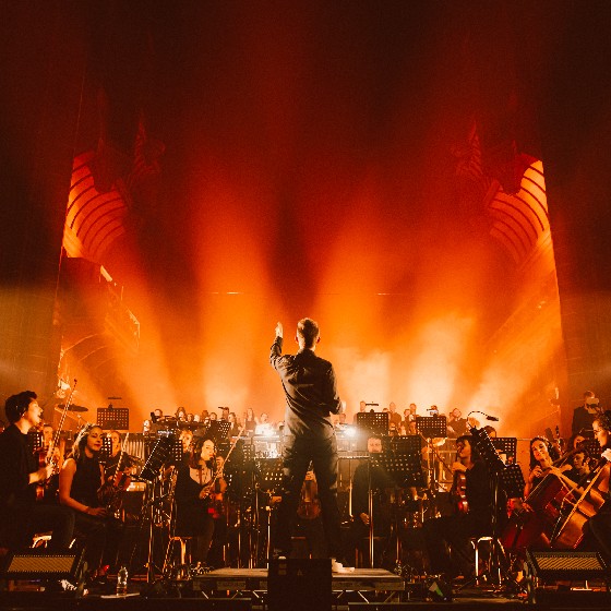 An orchestra performing on stage with dramatic orange lighting behind them