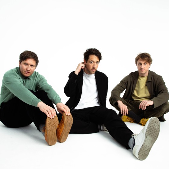 The Wombats, a band of three men, sat on the floor in a white room