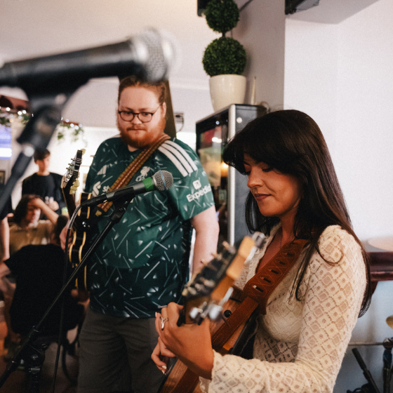 Two people paying guitars and standing behind microphones. 