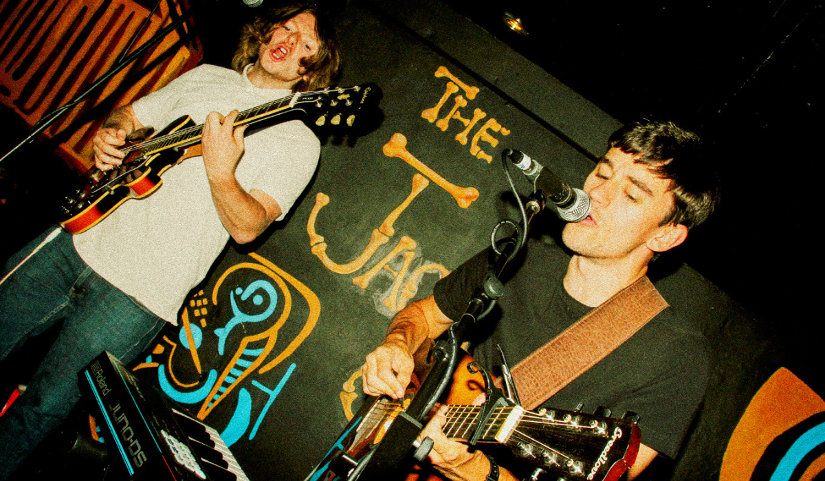 Two people singing on a stage holding guitars.