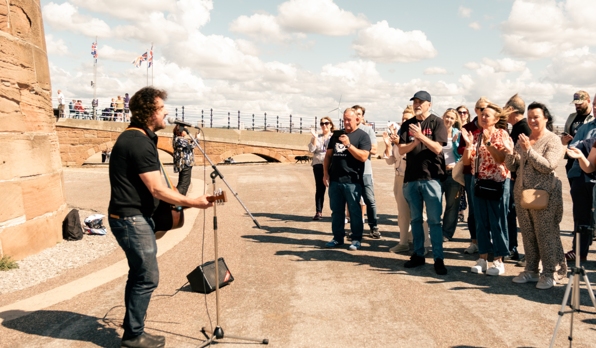 A photo of a person playing guitar to a crowd of people at a beach.