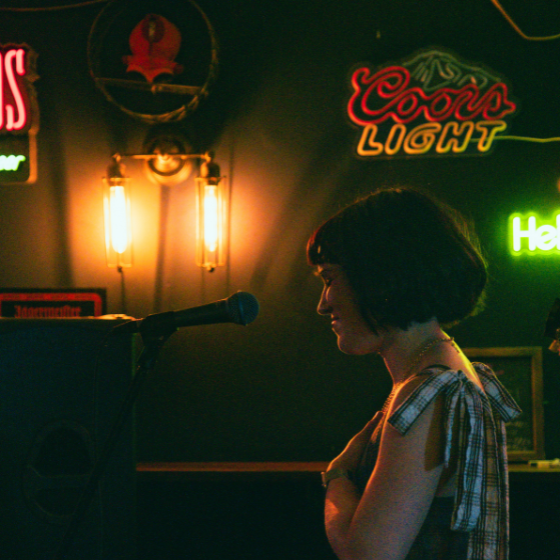 A side profile of a person in a dark bar with lights on the wall behind them.