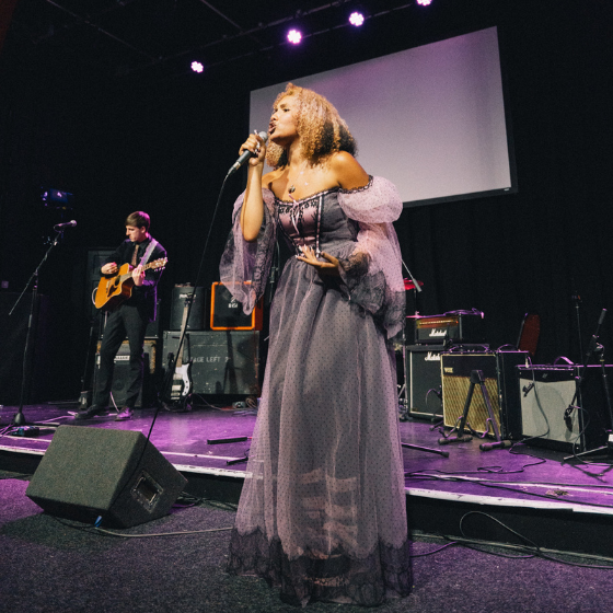 A person on a stage wearing a grey dress singing.