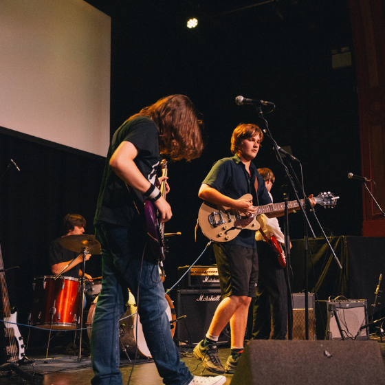 four people on a stage in a band playing guitars and drums.